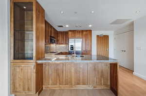 Kitchen featuring a peninsula, brown cabinets, backsplash, stainless steel appliances, and light wood-style floors