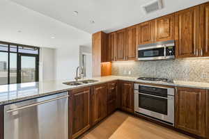 Kitchen with appliances with stainless steel finishes, light stone countertops, light wood finished floors, decorative backsplash, and recessed lighting