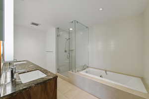 Bathroom featuring a bath, a shower stall, light tile patterned floors, double vanity, and recessed lighting