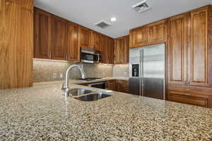 Kitchen with appliances with stainless steel finishes, brown cabinets, light stone counters, tasteful backsplash, and recessed lighting