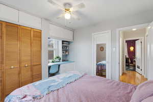 Bedroom featuring built in study area, a closet, a ceiling fan, and wood finished floors