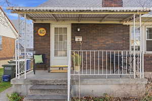 View of exterior entry featuring brick siding, a chimney, a shingled roof, and crawl space