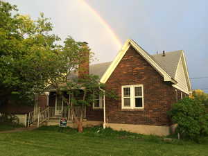 Back of house with brick siding, roof with shingles, a chimney, and a yard