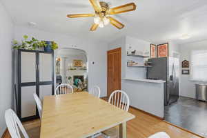 Dining room featuring arched walkways, light wood-style floors, a fireplace, and a ceiling fan