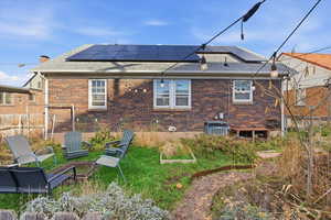 Back of house featuring roof with shingles, roof mounted solar panels, and brick siding