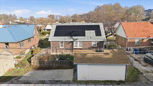 View of front of home with a fenced backyard, brick siding, solar panels, and roof with shingles
