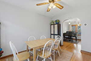 Dining area with light wood-type flooring, arched walkways, and ceiling fan