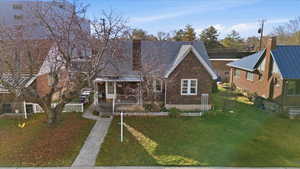 View of front of house featuring a chimney, covered porch, brick siding, and a metal roof