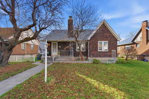Bungalow featuring brick siding, a porch, a chimney, and a front yard
