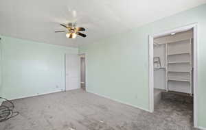 Unfurnished bedroom featuring a spacious closet, carpet flooring, and a ceiling fan