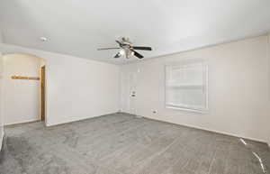 Empty room with carpet, arched walkways, and ceiling fan