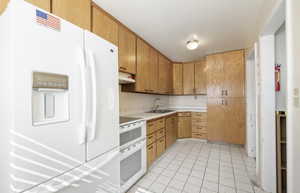 Kitchen featuring white appliances, light countertops, brown cabinets, light tile patterned floors, and under cabinet range hood