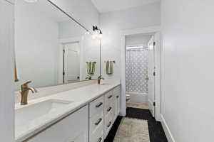 Bathroom featuring double vanity, shower / tub combo, and dark tile patterned flooring