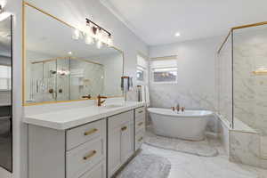 Full bathroom featuring tile walls, vanity, wainscoting, a freestanding bath, and light marble finish floors