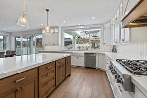 Kitchen featuring glass insert cabinets, decorative light fixtures, appliances with stainless steel finishes, brown cabinets, and white cabinets