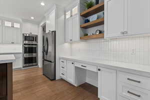 Kitchen with open shelves, glass insert cabinets, white cabinets, stainless steel appliances, and backsplash