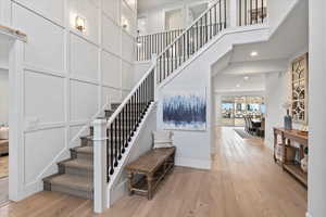 Staircase with a towering ceiling, recessed lighting, wood-type flooring, and a decorative wall