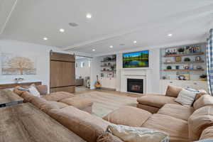 Living area featuring a barn door, recessed lighting, beamed ceiling, a lit fireplace, and built in features