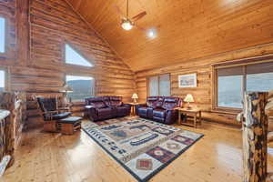 Living room featuring high vaulted ceiling, wooden ceiling, light wood-style flooring, log walls, and a ceiling fan