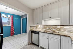 Kitchen with white cabinets, light stone counters, stainless steel dishwasher, and light tile patterned floors