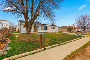 Single story home featuring roof mounted solar panels and a fenced front yard