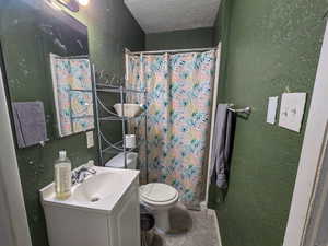 Bathroom featuring a textured wall, a stall shower, a textured ceiling, vanity, and tile patterned flooring