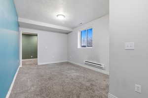 Unfurnished room with a baseboard heating unit, a textured ceiling, and light carpet