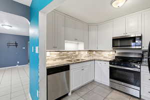 Kitchen with stainless steel appliances, a textured ceiling, light tile patterned floors, light stone counters, and white cabinets