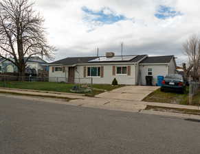 Ranch-style home featuring solar panels, a fenced front yard, concrete driveway, and roof with shingles