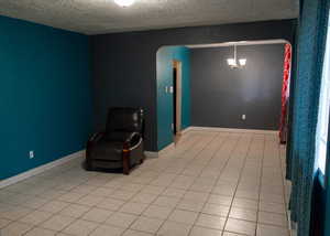 Unfurnished room featuring arched walkways, a textured ceiling, light tile patterned floors, and a chandelier