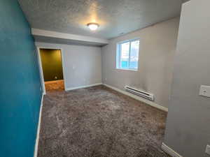 Carpeted spare room with a textured ceiling and baseboard heating