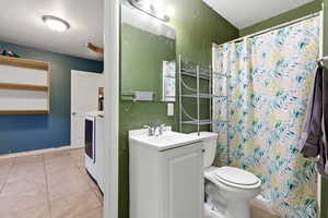 Bathroom with vanity, a shower with curtain, light tile patterned flooring, a textured wall, and washer / clothes dryer