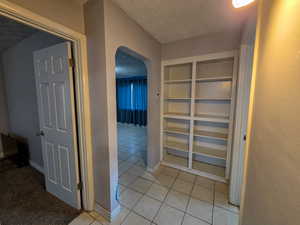 Corridor with arched walkways, a textured ceiling, light tile patterned flooring, built in shelves, and light colored carpet