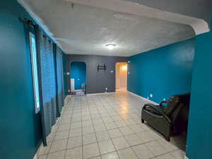 Unfurnished living room featuring arched walkways, a textured ceiling, and light tile patterned floors