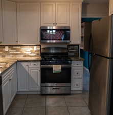 Kitchen featuring appliances with stainless steel finishes, dark stone countertops, light tile patterned floors, and white cabinets