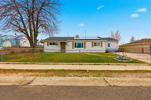 Single story home with solar panels and a fenced front yard