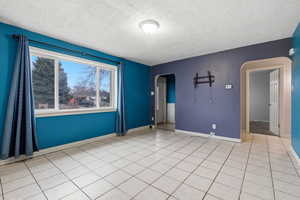 Unfurnished room with arched walkways, a textured ceiling, and light tile patterned floors