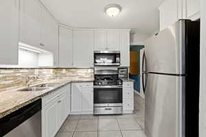 Kitchen featuring stainless steel appliances, light stone counters, white cabinetry, and light tile patterned flooring