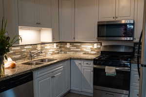 Kitchen with appliances with stainless steel finishes, dark stone countertops, backsplash, and tile patterned floors