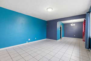 Unfurnished room with arched walkways, a textured ceiling, and light tile patterned floors