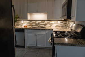 Kitchen with stainless steel appliances, dark stone counters, light tile patterned floors, and tasteful backsplash