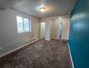 Spare room with dark colored carpet, a textured ceiling, arched walkways, and baseboard heating