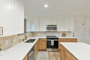 Kitchen featuring appliances with stainless steel finishes, light wood-style flooring, white cabinets, backsplash, and recessed lighting