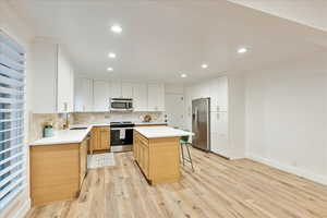 Kitchen featuring appliances with stainless steel finishes, a kitchen bar, white cabinets, a kitchen island, and light wood-style floors