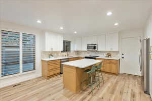 Kitchen featuring stainless steel appliances, light wood-style floors, white cabinetry, a breakfast bar area, and recessed lighting