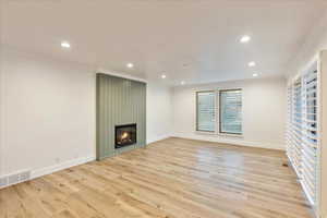 Unfurnished living room featuring a fireplace, crown molding, light wood finished floors, and recessed lighting