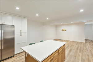 Kitchen featuring stainless steel refrigerator, light wood-type flooring, hanging light fixtures, recessed lighting, and a kitchen island