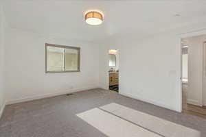 Unfurnished bedroom featuring light colored carpet, crown molding, and connected bathroom