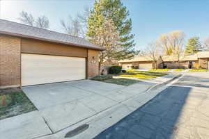 View of property exterior with brick siding, driveway, a shingled roof, a garage, and a residential view
