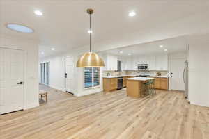 Kitchen with a breakfast bar area, recessed lighting, light wood finished floors, decorative backsplash, and pendant lighting